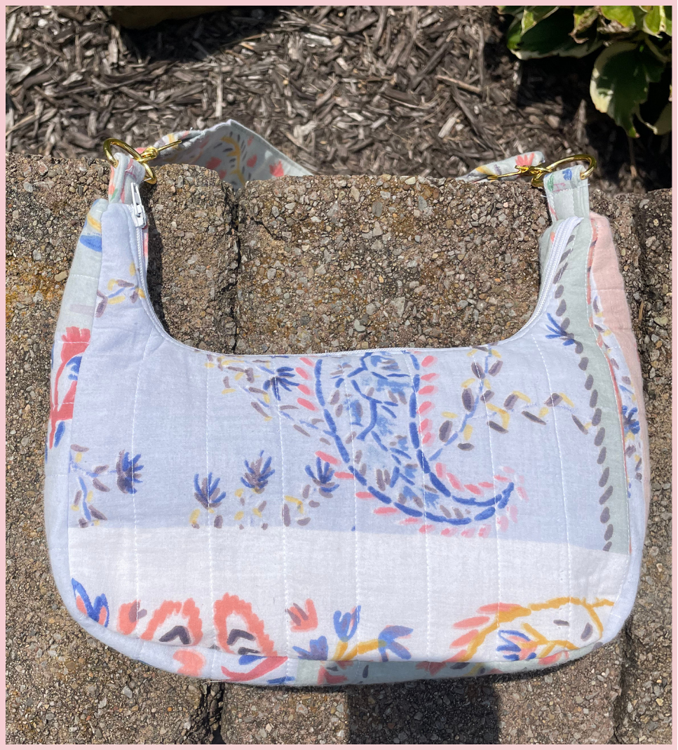 A quilted fabric shoulder bag with a floral and paisley print, resting on a concrete surface outdoors.