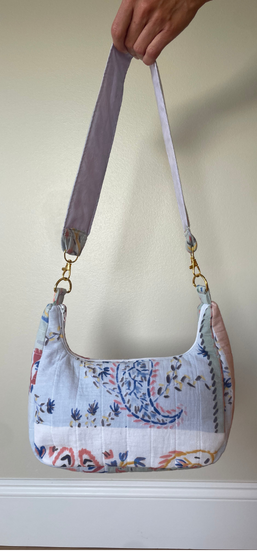 A handmade shoulder bag made from patterned quilted cotton fabric, held by a hand against a plain beige wall.