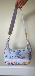 A handmade shoulder bag made from patterned quilted cotton fabric, held by a hand against a plain beige wall.