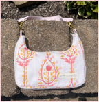 A white quilted fabric shoulder bag with a pink and orange botanical pattern, resting on a textured concrete surface outdoors.