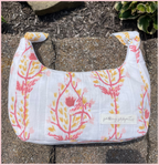 A small fabric shoulder bag with a white background and a pink and yellow botanical pattern, resting on a stone surface outdoors. A small fabric label on the front reads 'petty projects'.