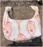 A white shoulder bag with a pink and yellow botanical pattern, photographed outdoors on a concrete surface with mulch in the background.