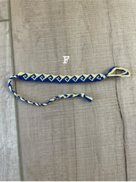 A blue and white braided rope accessory with a gold metal clasp, laid flat on a textured gray fabric background.