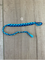 A blue and black braided friendship bracelet with a tassel, laid out on a light brown wood-grain surface.