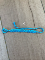 A bright blue braided rope bracelet with a small tassel and a white letter 'J' charm, displayed on a brown wooden surface.