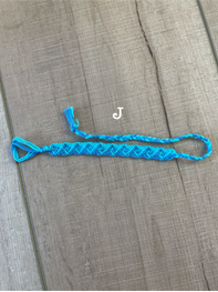 A bright blue braided rope bracelet with a small tassel and a white letter 'J' charm, displayed on a brown wooden surface.