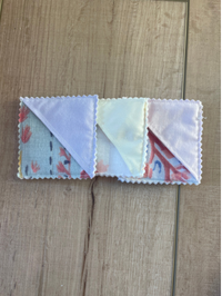 Three small square fabric pouches or card cases with scalloped edges, shown on a light wood surface. The fabrics have different prints, including pale blue, pale yellow, and pink floral patterns.