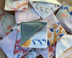 A pile of small triangular fabric napkins or pocket squares with floral and abstract prints, arranged on a wooden surface.