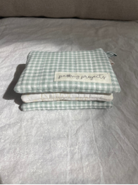 A folded light green and white gingham checkered fabric pouch or small bag with a small white label, resting on a light gray textured fabric surface.