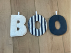 Three fabric face masks in different designs laid out vertically on a light wood floor: a white mask at the top, a black-and-white striped donut-shaped mask in the middle, and a solid dark navy donut-shaped mask at the bottom.