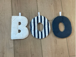 Three fabric face masks in different designs laid out vertically on a light wood floor: a white mask at the top, a black-and-white striped donut-shaped mask in the middle, and a solid dark navy donut-shaped mask at the bottom.