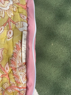 A close-up of a quilted blanket or comforter showing a yellow floral pattern with pink and peach details, a pink border, and a white stitched label that reads 'Sporkhead Quilted'.
