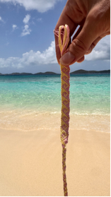 A close-up of a hand holding a thick tan rope against a tropical beach background with turquoise water and a blue sky.